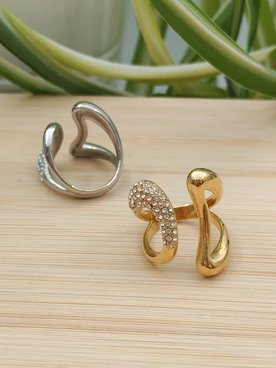 Bagues en acier inoxydable ouvertes, une dorée sertie de strass et une argentée, au design moderne et élégant, posées sur une surface en bois.