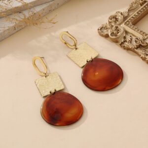 Boucles d’oreilles pendantes en acier inoxydable doré, avec carré texturé et pendentif ambre marbré, présentées sur fond beige avec cadre doré et éléments naturels – bijou artistique et élégant pour femme.