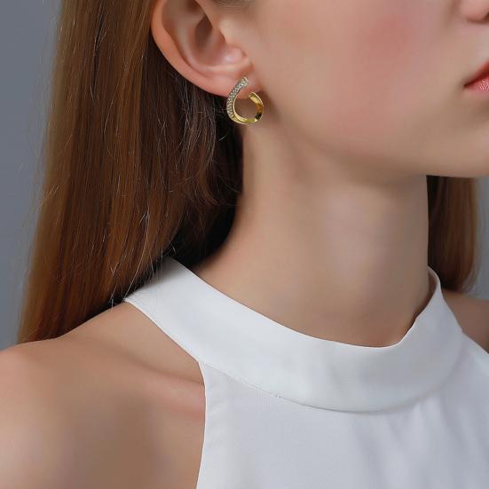 Boucle d’oreille Alyra portée par une personne vêtue d’un haut blanc à col montant. Le bijou combine des tons dorés et argentés, avec des pierres scintillantes sur la partie supérieure. Les cheveux sont lissés et dégagés derrière l’oreille, sur fond neutre.