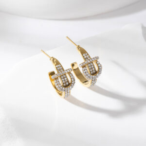 Boucles d’oreilles Diora en acier inoxydable doré, ornées de pierres scintillantes et d’un motif inspiré d’une boucle de ceinture, présentées sur fond blanc avec une lumière douce qui met en valeur leur brillance et leur design audacieux.