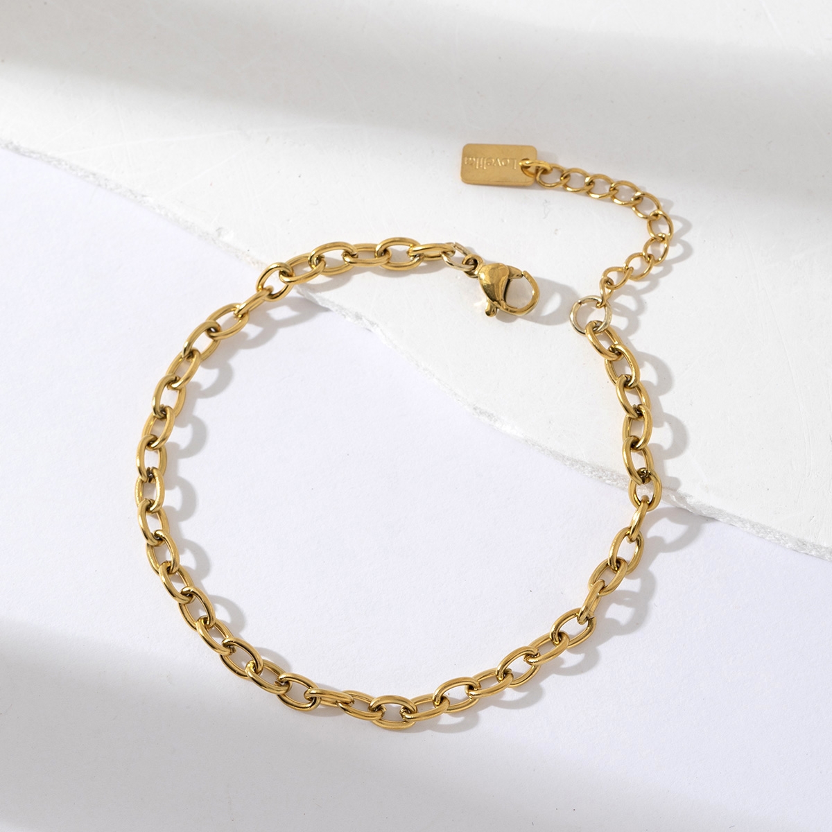 Bracelet gourmette en acier inoxydable doré avec chaîne forçat et fermoir ajustable, présenté sur fond blanc texturé – bijou minimaliste et élégant pour femme.