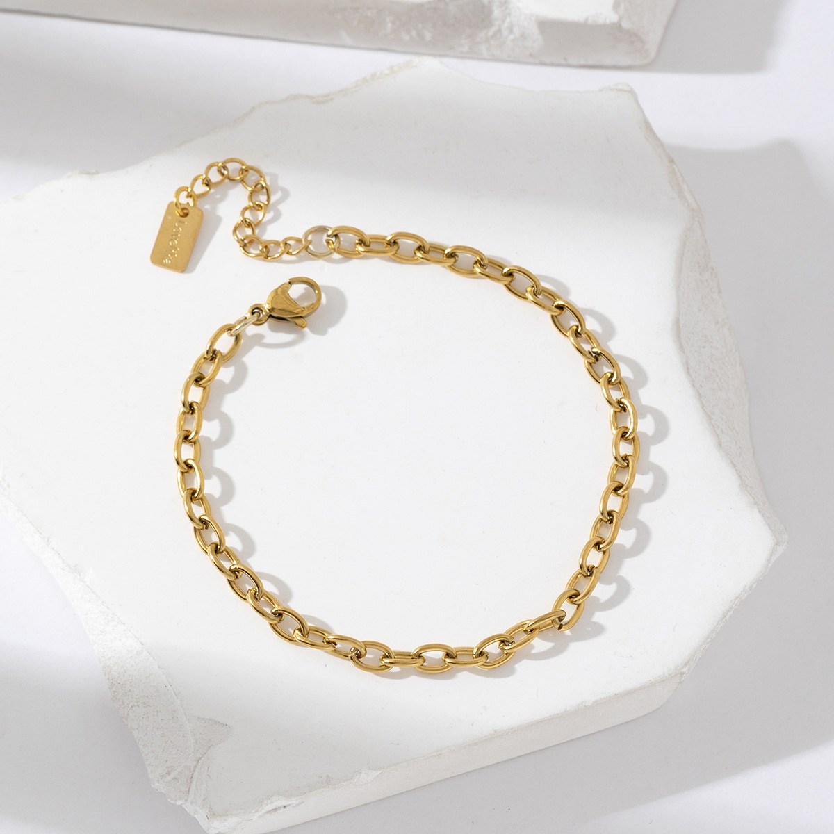 Bracelet gourmette en acier inoxydable doré avec chaîne forçat et fermoir ajustable, présenté sur fond blanc texturé – bijou minimaliste et élégant pour femme.