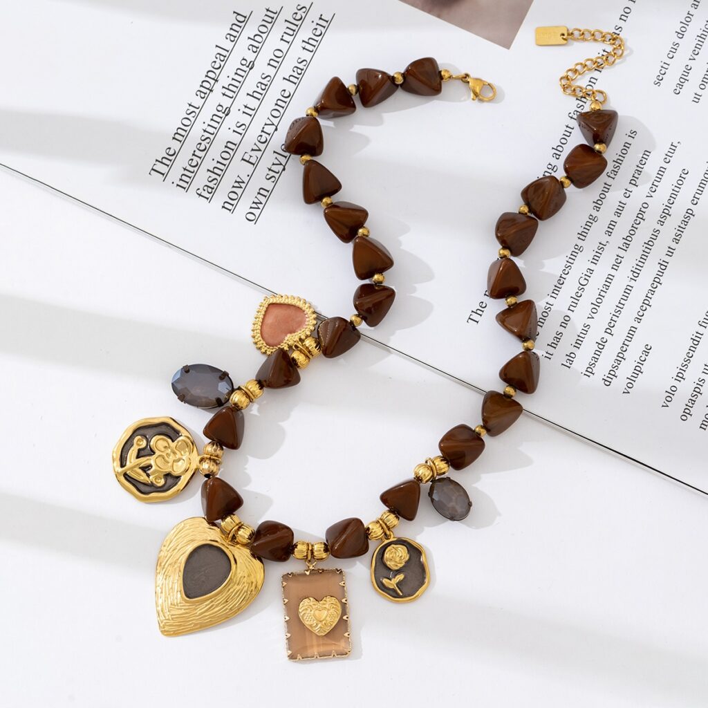Collier fantaisie en acier inoxydable avec pendentifs dorés en forme de cœur et perles brunes, présenté sur fond blanc avec vaisselle en céramique – bijou romantique et durable pour femme.