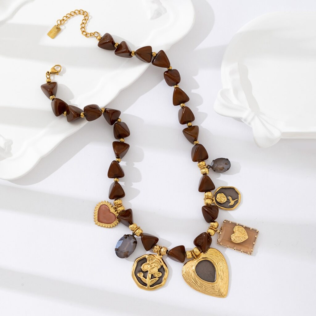 Collier fantaisie en acier inoxydable avec pendentifs dorés en forme de cœur et perles brunes, présenté sur fond blanc avec vaisselle en céramique – bijou romantique et durable pour femme.