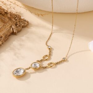 Collier fantaisie en acier inoxydable avec pendeloques Cristaux sur chaîne en maillon fin, présenté sur fond beige avec cadre doré et décor organique – bijou élégant et intemporel pour femme.