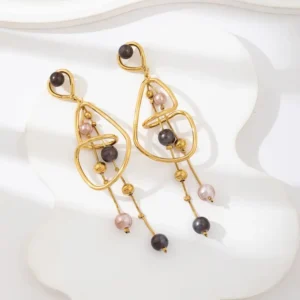 Boucles d’oreilles Bluma dorées avec perles colorées sur fond blanc en tissu, au style sculptural et moderne.
