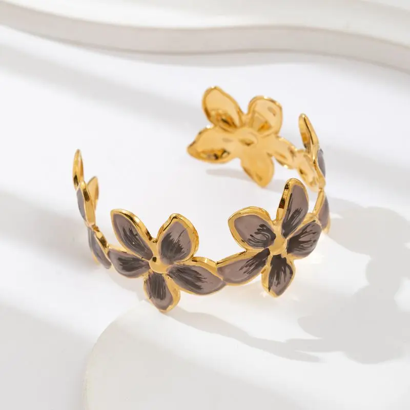 Bracelet jonc doré à motif floral avec centres foncés, posé sur fond beige élégant.