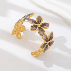Bracelet jonc doré à motif floral avec centres foncés, posé sur fond beige élégant.