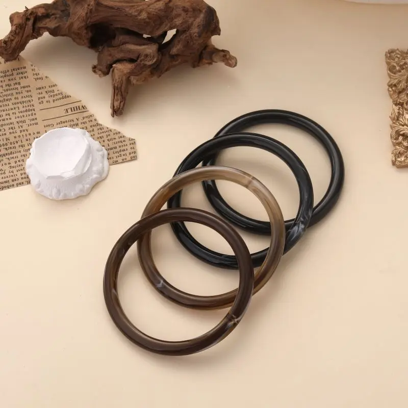 Bracelets jonc Augustine en résine brillante, disponibles en plusieurs couleurs naturelles, posés sur fond beige avec éléments décoratifs.