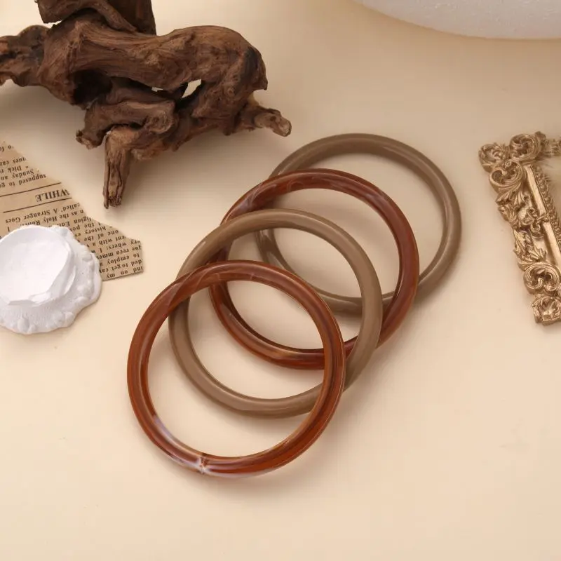 Bracelets jonc Augustine en résine brillante, disponibles en plusieurs couleurs naturelles, posés sur fond beige avec éléments décoratifs.