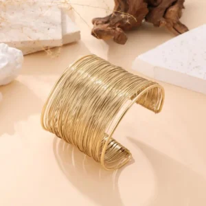 Bracelet jonc Lena en métal doré tressé, posé sur fond beige avec éléments naturels.