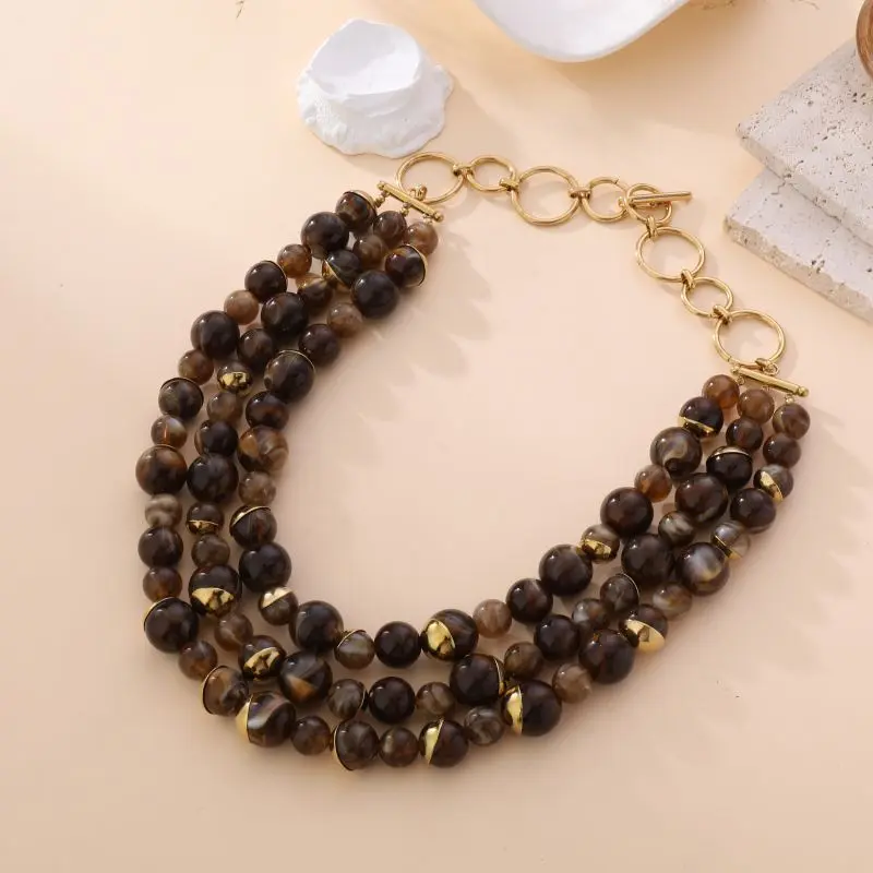 Collier multi-rangs Laura avec perles brunes et fumées, accents dorés et fermoir en anneaux, bijou élégant sur fond beige