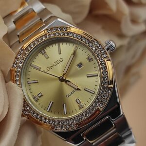 Montre LONGBO à cadran doré avec bracelet bicolore argent et or, lunette sertie de cristaux brillants, posée sur un fond de fleurs beige.