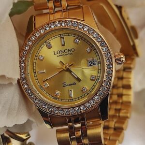Montre LONGBO entièrement dorée avec cadran doré, lunette sertie de cristaux et bracelet métallique, posée sur un fond de pétales crème.