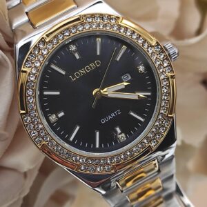 Montre LONGBO à cadran noir avec index dorés et pierres brillantes, lunette sertie de cristaux, bracelet métallique bicolore argent et or, posée sur un fond floral beige.